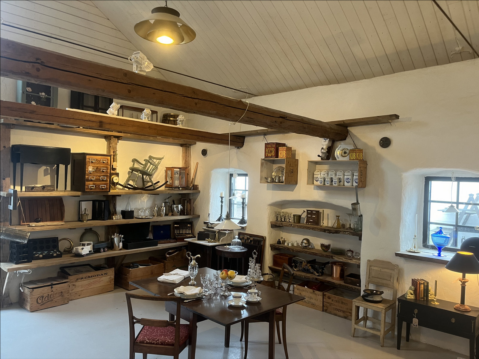 Butiken hos Alla Tiders: hyllor fulla av vintage, ett dukat bord och ljus från fönstret